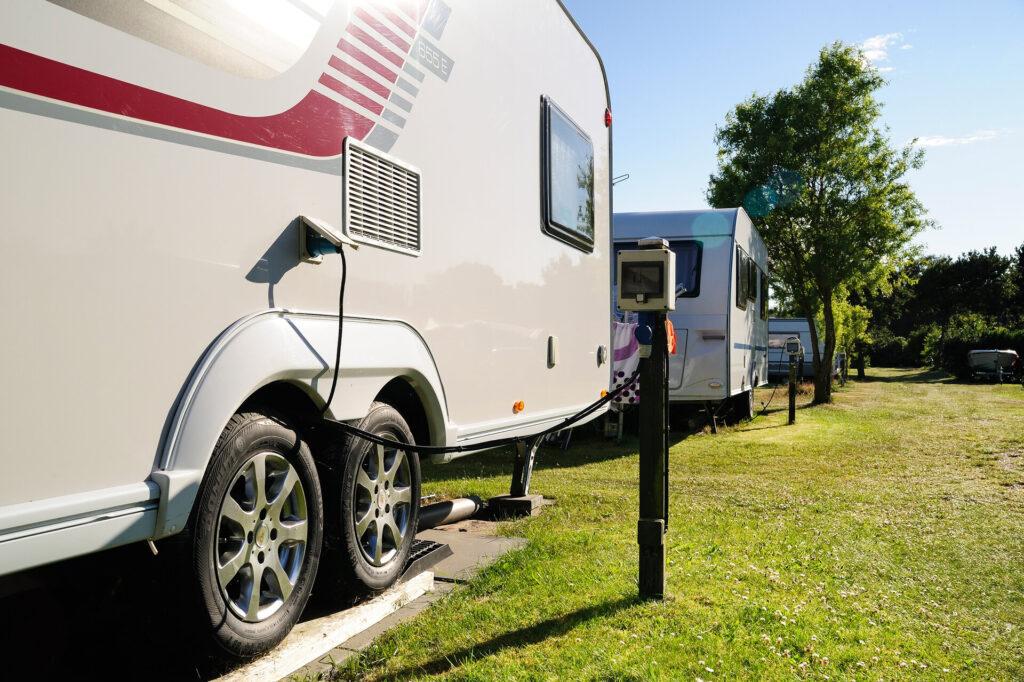 E-Wohnwagen lädt an einer Steckdose auf einem Campingplatz