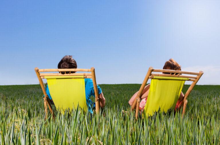 Zwei Menschen liegen auf Liegen im Feld und entspannen bei strahlendem Sonnenschein