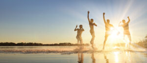 Glückliche junge Menschen laufen und springen am Strand in der Sonne