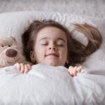 Ein kleines Mädchen schläft in einem weißen, gemütlichen Bett und mit einer weichen Decke.